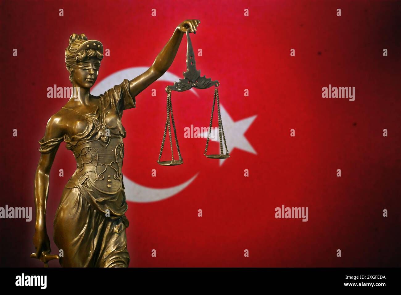 Primo piano di una piccola statuetta di bronzo di Lady Justice davanti a una bandiera turca. Foto Stock