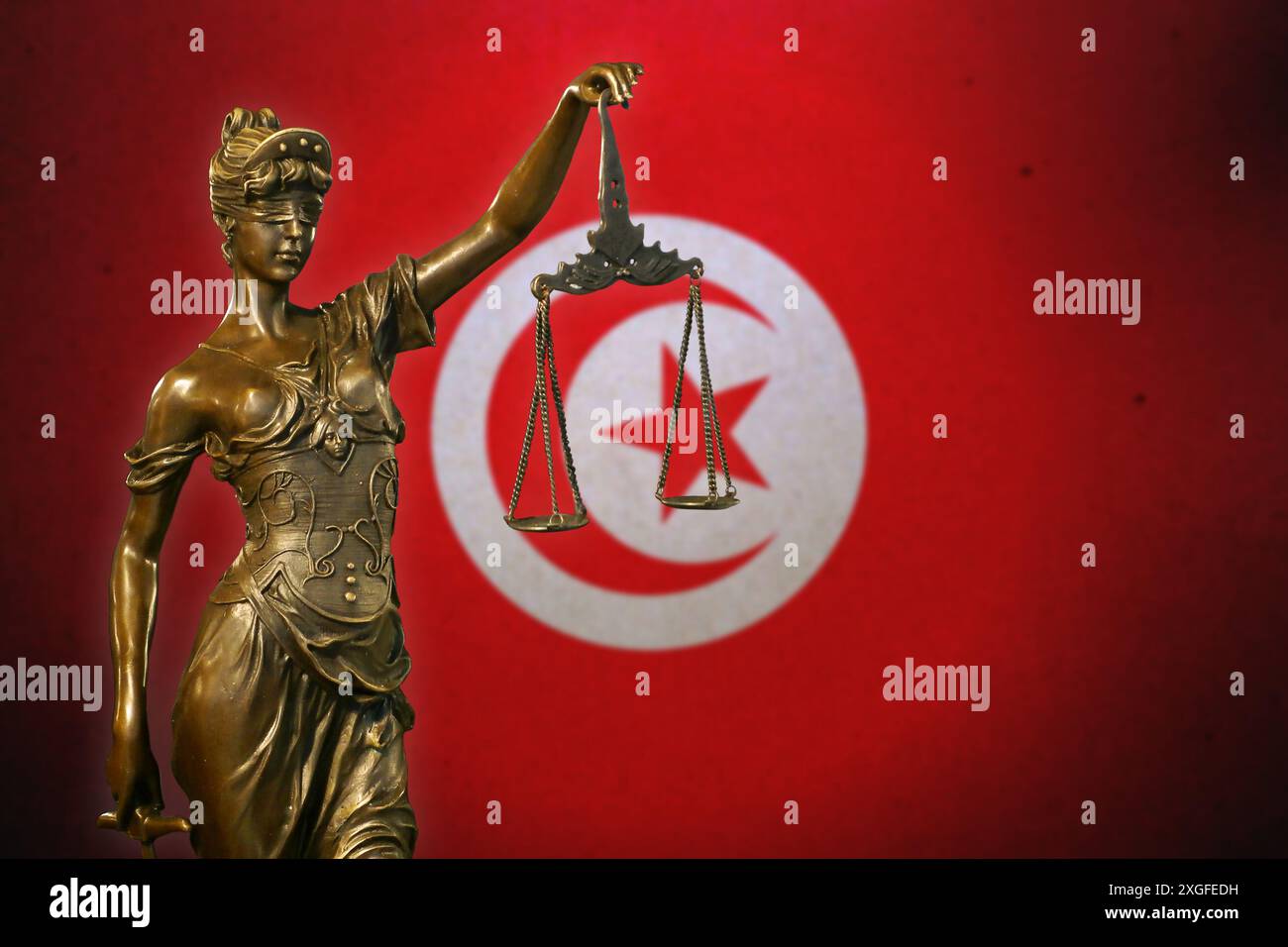 Primo piano di una piccola statuetta di bronzo di Lady Justice davanti a una bandiera tunisina. Foto Stock