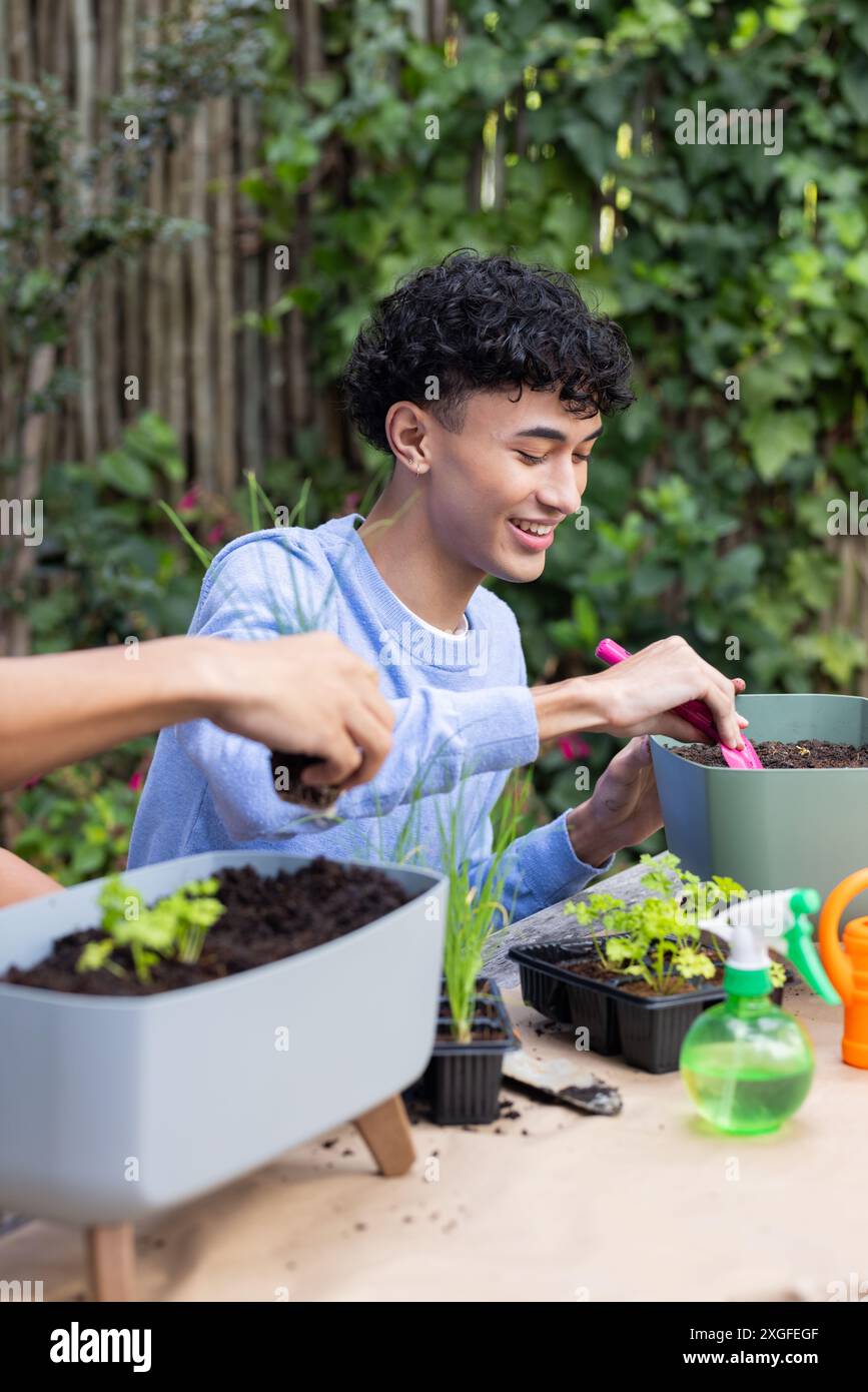 Giardinaggio a casa, giovane piantare piantine in pentole, sorridere e divertirsi Foto Stock