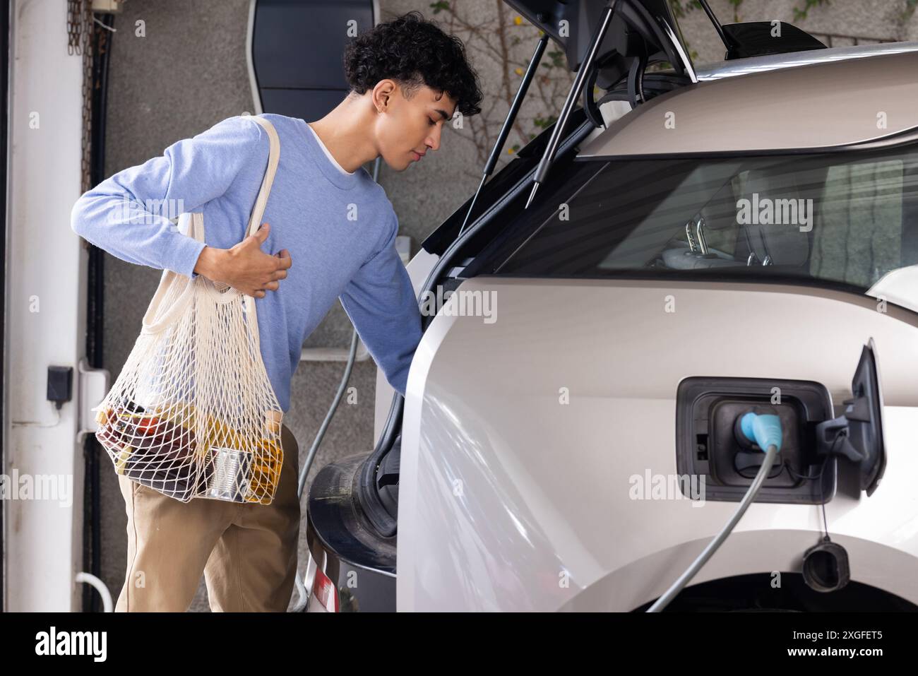 Scaricare la spesa dall'auto mentre si ricarica un'auto elettrica in garage Foto Stock