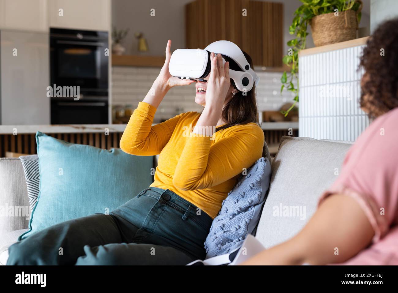 Utilizzando il visore VR, una donna seduta sul divano e godendo di un'esperienza di realtà virtuale Foto Stock