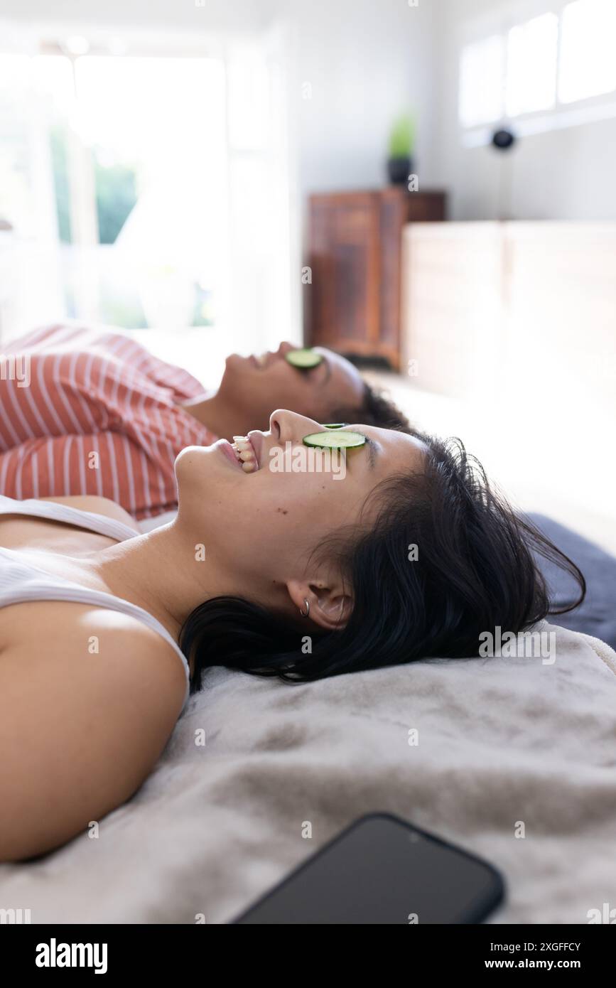 Rilassatevi a casa, le donne amiche con fette di cetriolo sugli occhi, godendovi una giornata in spa Foto Stock