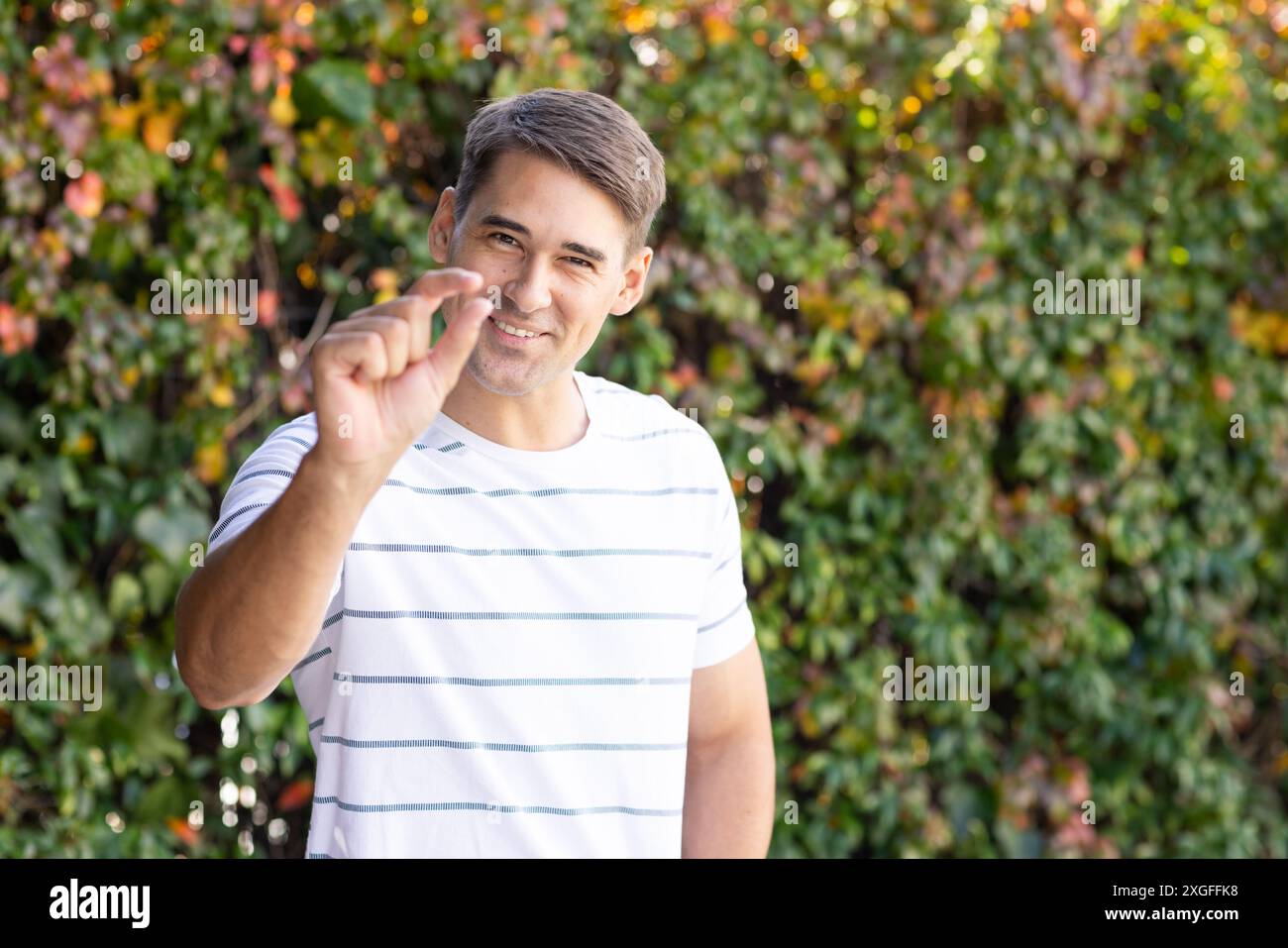 Uomo sorridente in camicia a righe che tiene piccoli oggetti all'aperto in giardino Foto Stock