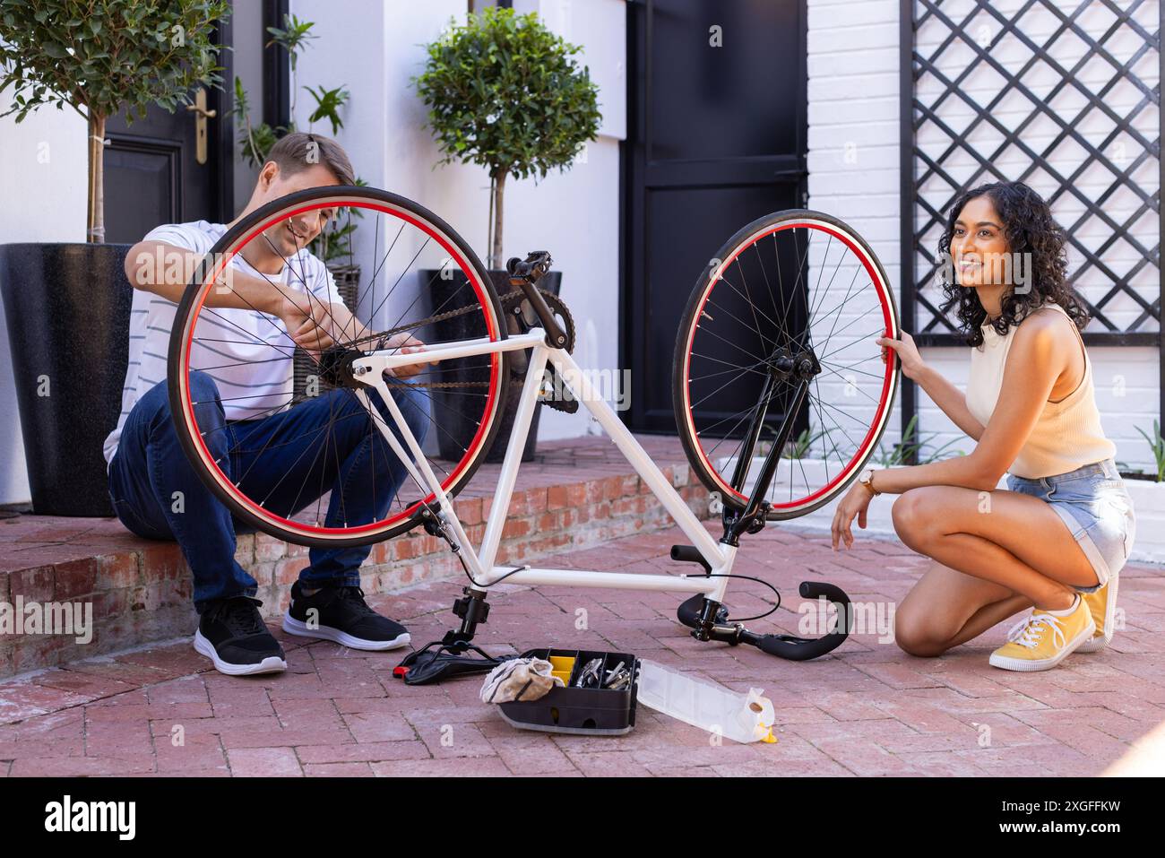 Riparando la bicicletta insieme, giovani coppie che si divertono all'aperto nelle giornate di sole Foto Stock