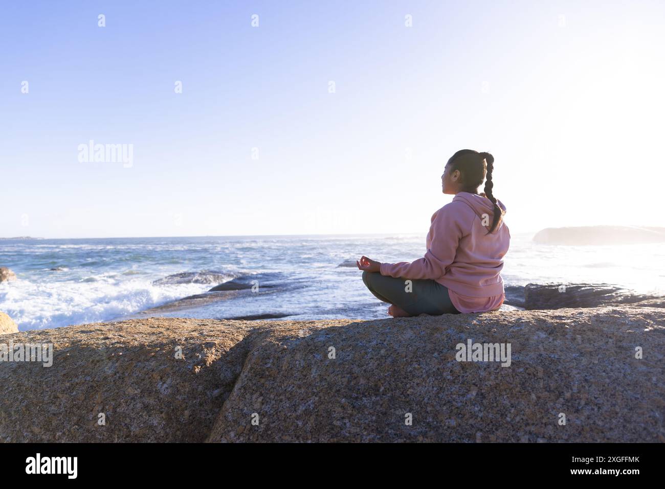 Meditando sulla roccia vicino all'oceano, donna che pratica la consapevolezza e le tecniche di rilassamento, copia lo spazio Foto Stock
