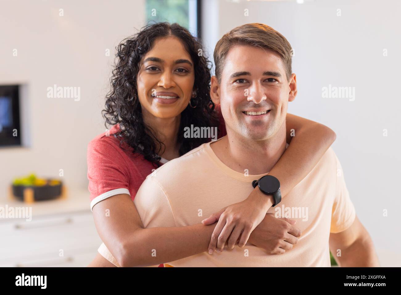 Una giovane coppia sorridente che si abbraccia a vicenda in un ambiente accogliente Foto Stock