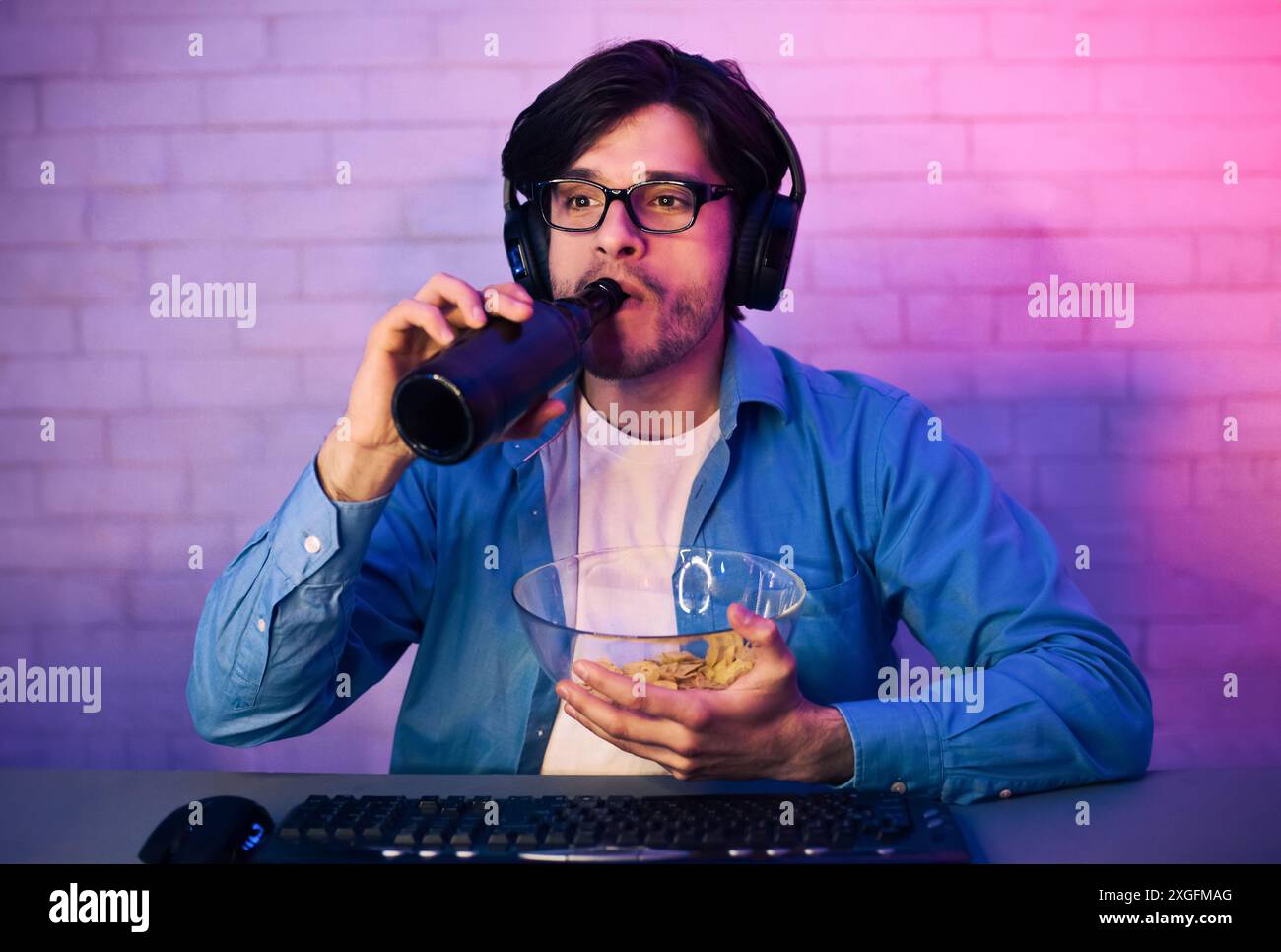 Il giovane beve birra, mangia patatine mentre gioca di notte Foto Stock