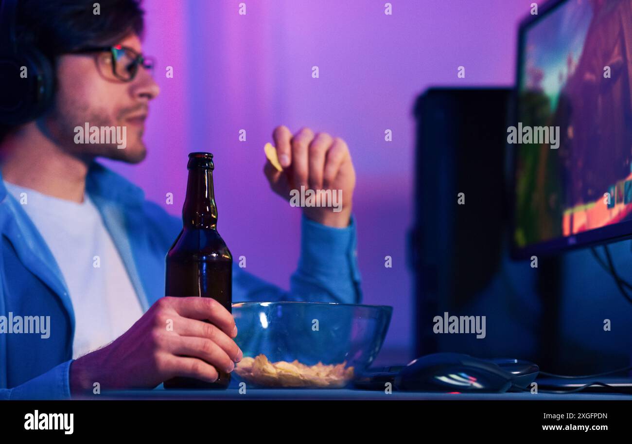 Uomo che gioca ai videogiochi con birra e patatine di notte Foto Stock