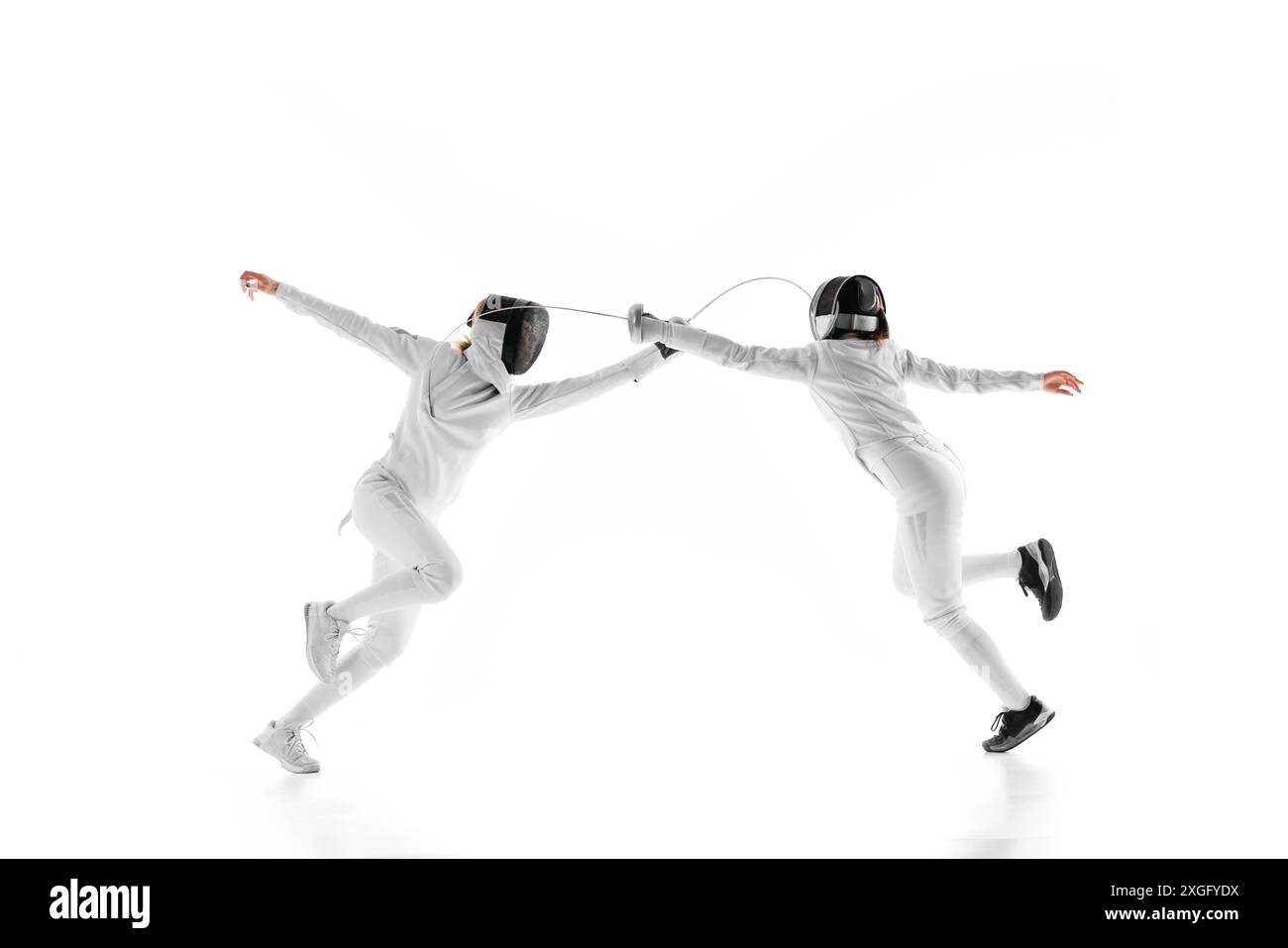 In preparazione per la partita, due fencer femminili vanno testa a testa, ognuna cercando di superare l'altra contro lo sfondo bianco dello studio. Movimento. Foto Stock