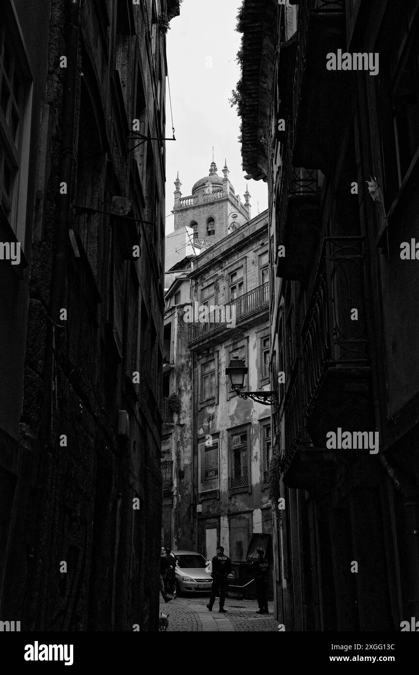 Lo stretto vicolo ombreggiato di Porto rivela i dettagli intricati degli edifici storici, che conducono a una coppia di poliziotti e a una torre della chiesa Foto Stock