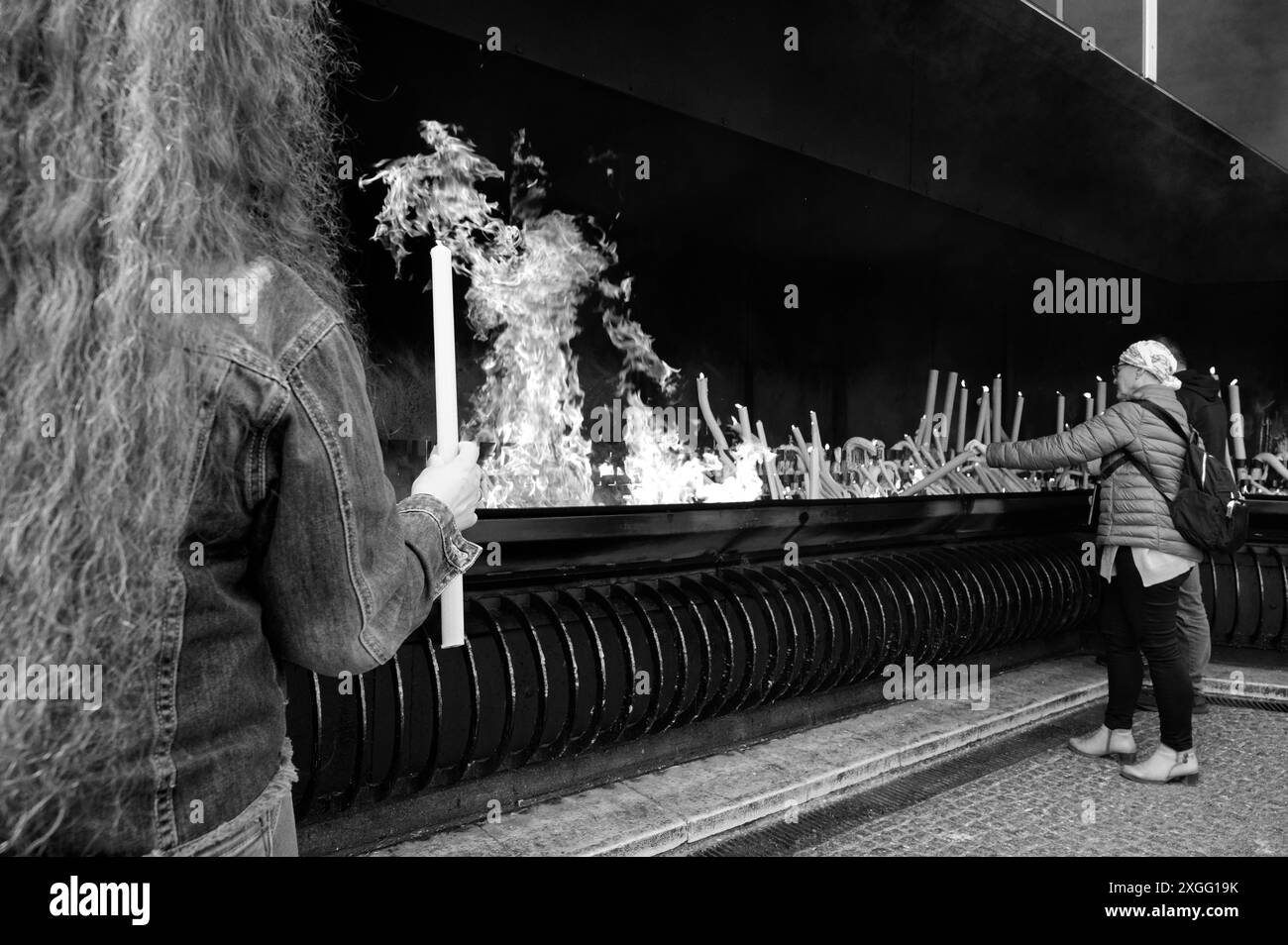 Una persona che indossa una bandana sopra la testa, accende una candela a una grande fiamma nel sito religioso di Fátima Foto Stock