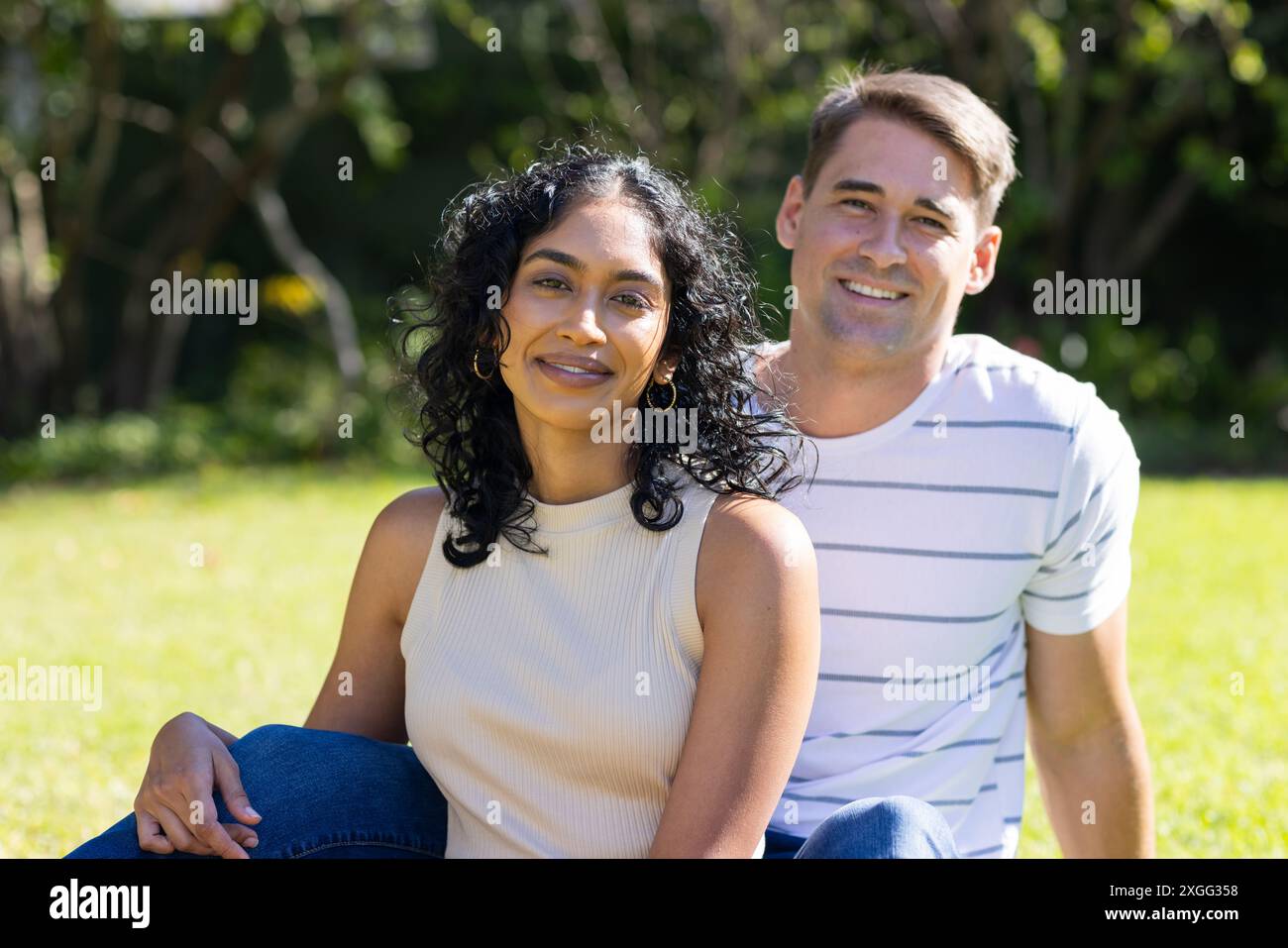 Giovane coppia sorridente seduta insieme sull'erba nel parco all'aperto Foto Stock