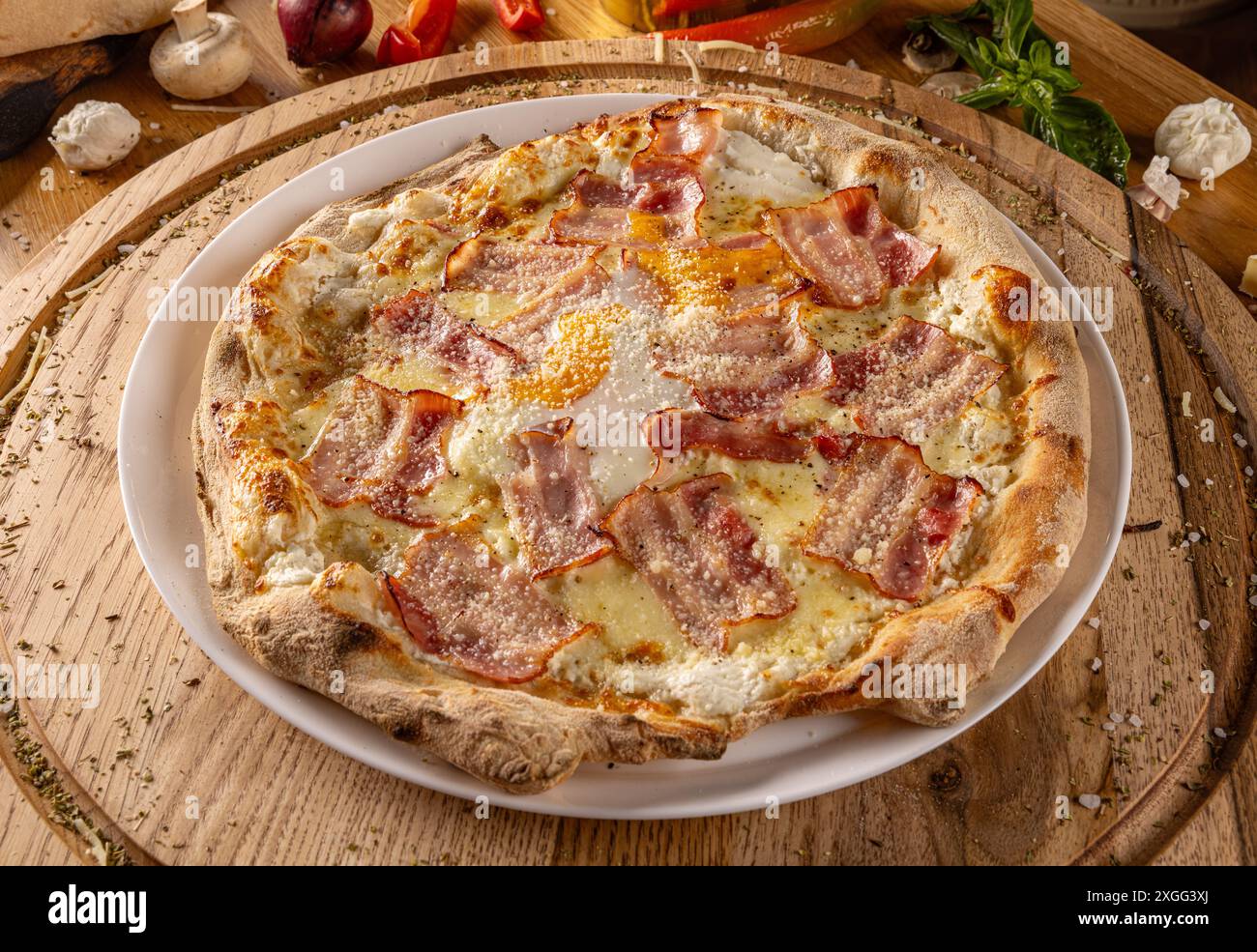 Pizza con pancetta fatta in casa circondata da ingredienti freschi su un tavolo da cucina in legno Foto Stock
