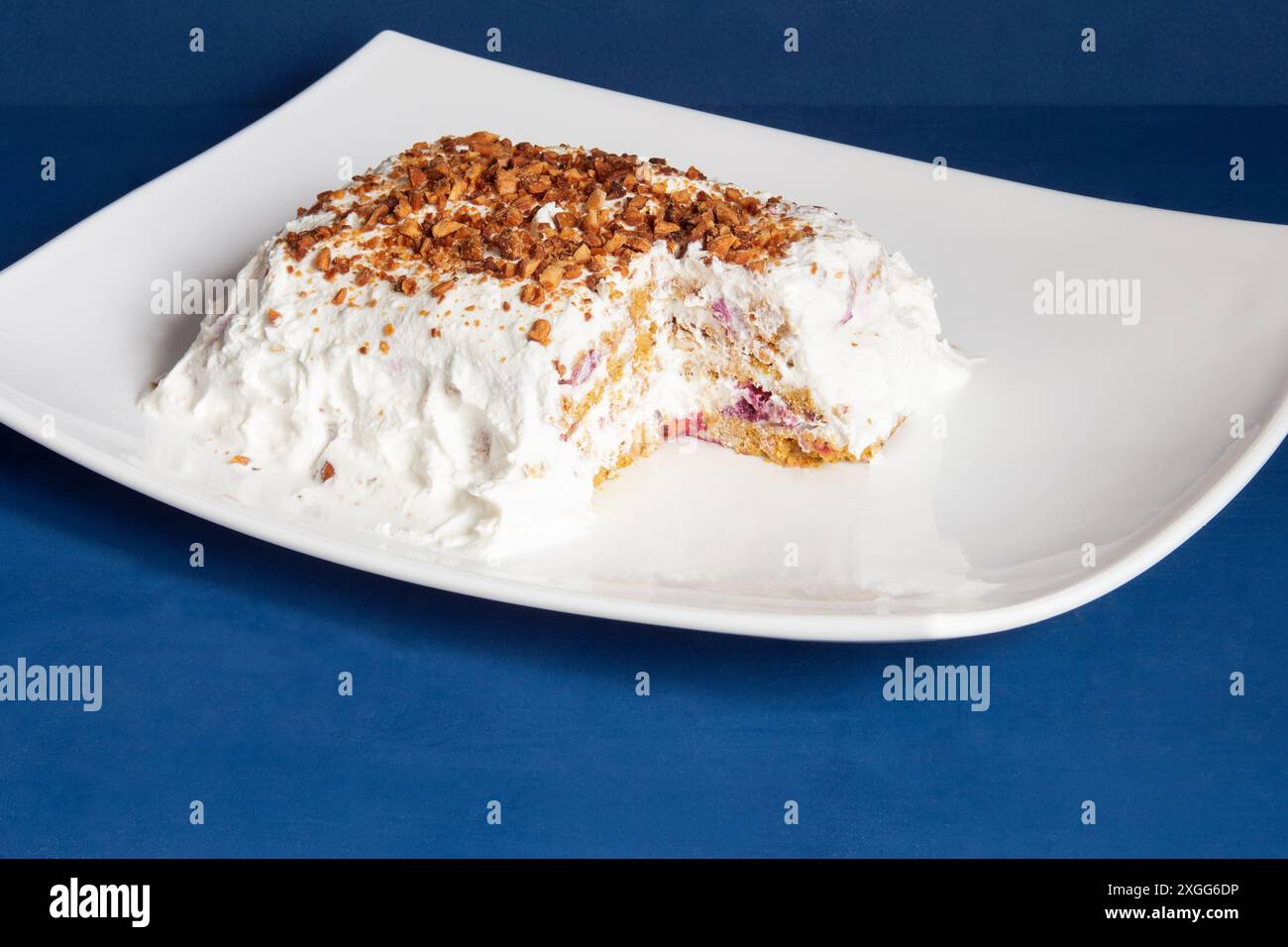 Delizioso dessert fatto in casa con una fetta parzialmente mangiata, rivelando il suo interno a strati servito su un piatto bianco incontaminato contro un profondi corteccia blu Foto Stock