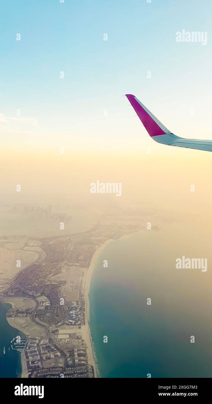 Dal punto di vista dei passeggeri, vista dalla finestra panoramica dello skyline di Abu Dhabi e della città con fiumi e paesaggi deserti al tramonto. Voli con compagnie aeree low budget holi Foto Stock