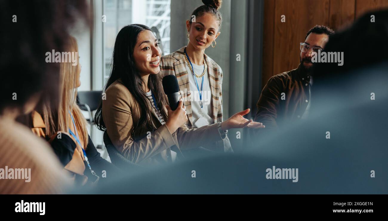 Donna che parla e partecipa a un dibattito con i colleghi durante una riunione di gruppo, condividendo idee e opinioni. Foto Stock