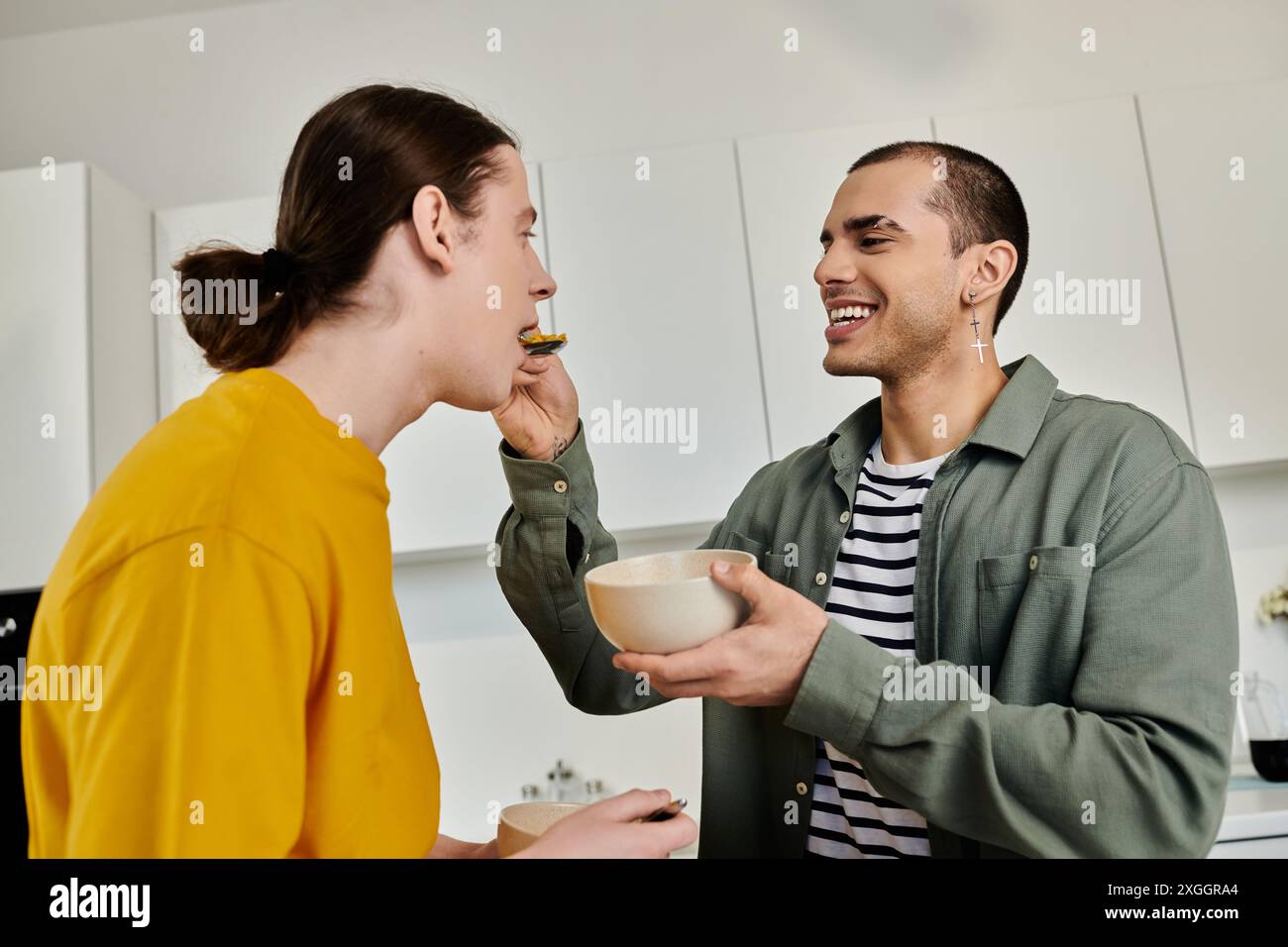 Una giovane coppia gay gode di un pasto insieme nel loro appartamento moderno, condividendo un momento di intimo legame. Foto Stock