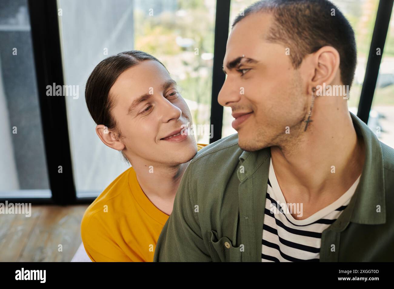 Due giovani gay in un abbigliamento casual condividono un look amorevole in un appartamento moderno. Foto Stock