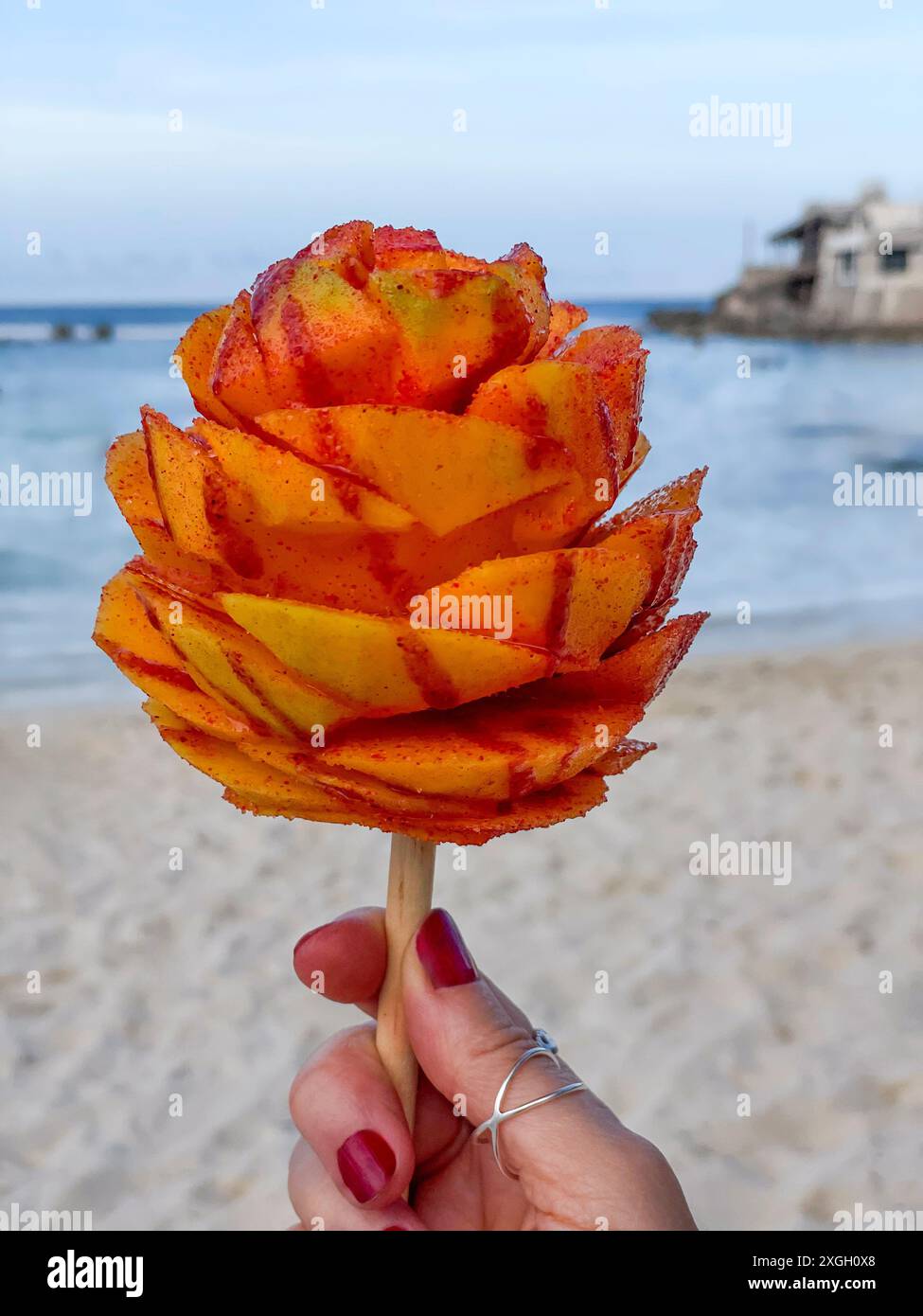 Mango su un bastoncino di legno tagliato come un fiore e cosparso di sale di peperoncino lime a Isla Mujeres, Messico. Taglio tradizionale del bastone di mango. Foto Stock