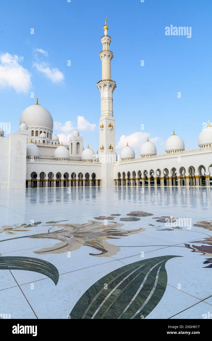 Abu Dhabi, Emirati Arabi Uniti - 4 gennaio 2024: La maestosa moschea dello sceicco Zayed sotto un cielo azzurro, che riflette la sua bellezza sul cortile lucido. Foto Stock