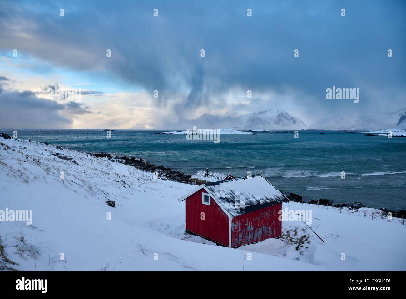 Capanna rossa nel paesaggio invernale con mare e montagne a Sandbotnen, Lofoten, Norvegia, Europa Foto Stock