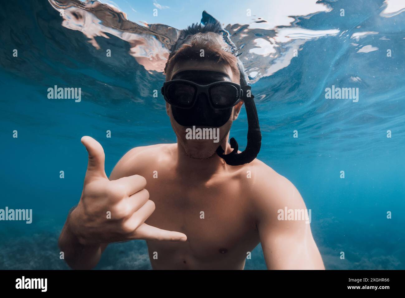 Il bellissimo subacqueo uomo libero in maschera mostra Shaka nell'oceano blu. Nuotare sott'acqua nel mare blu, selfie di un ragazzo sportivo Foto Stock