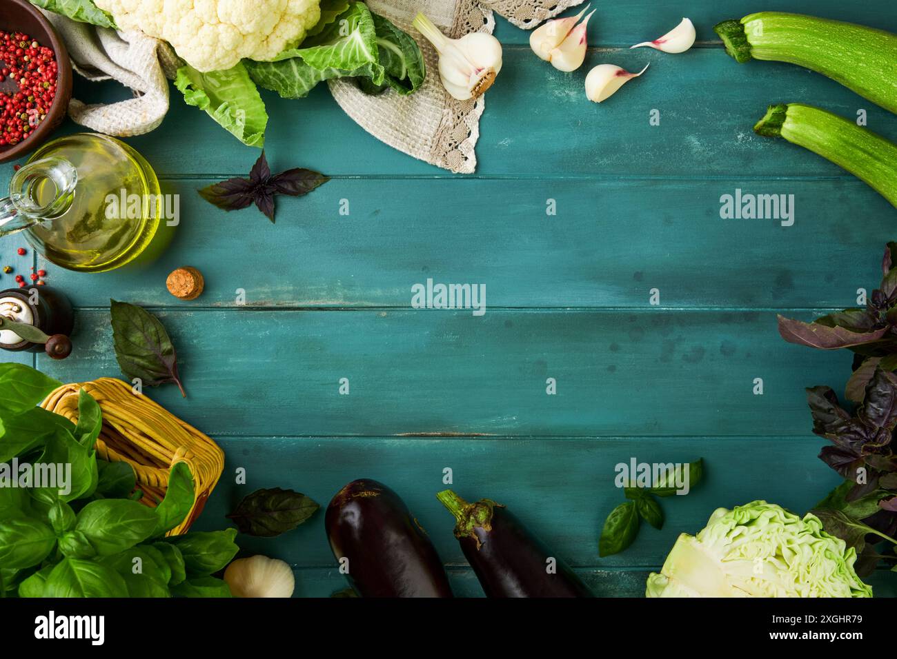 Sfondo rustico di cibo in legno bordo della cornice vuoto. Bordo culinario di un mazzo di basilico, cavolfiore, zucchine, aglio, olio d'oliva in bottiglia e pepe vecchio Foto Stock