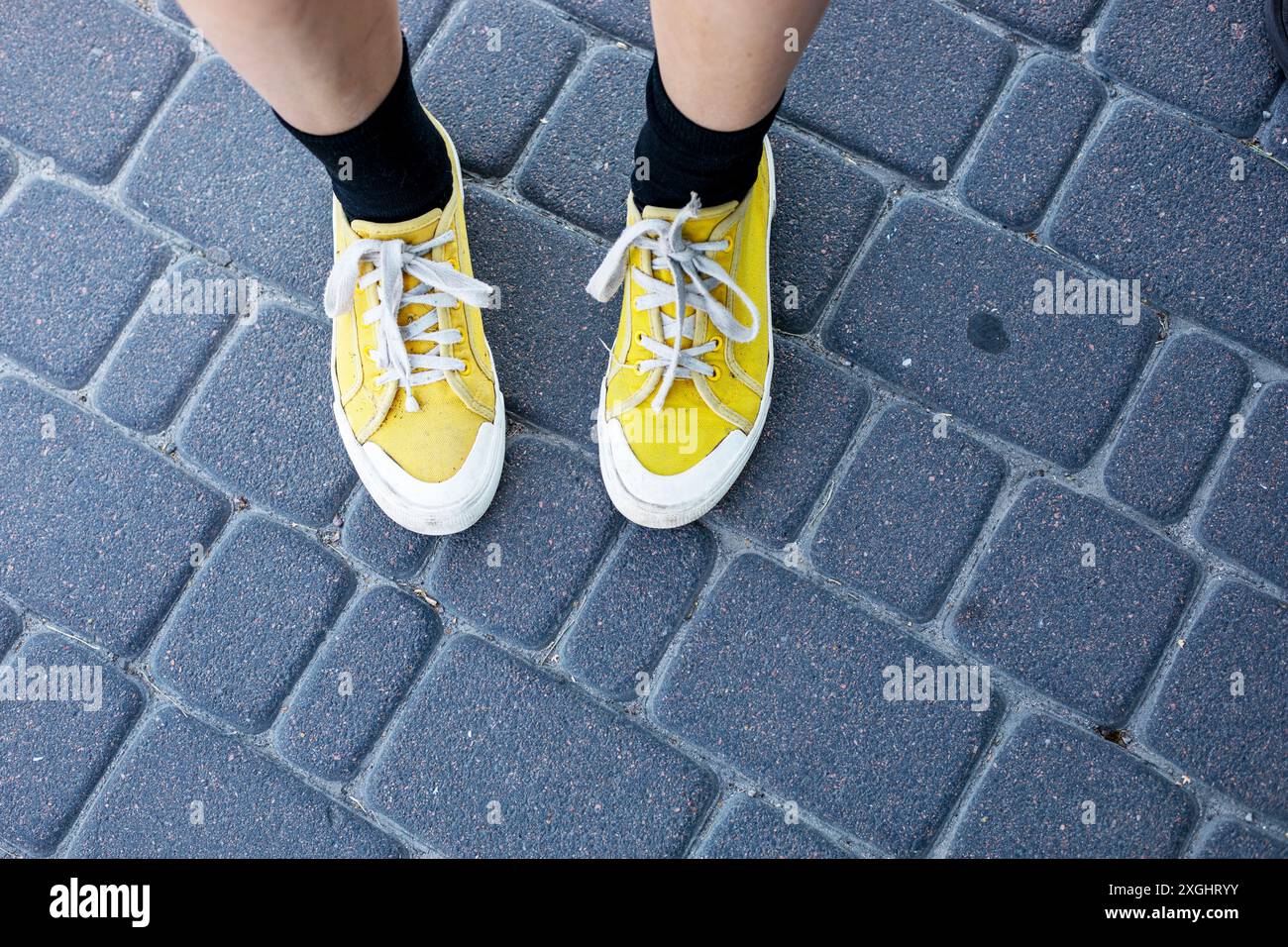 teenager con sneakers gialle si staglia sulle piastrelle della strada. Psicologia e sviluppo degli adolescenti Foto Stock