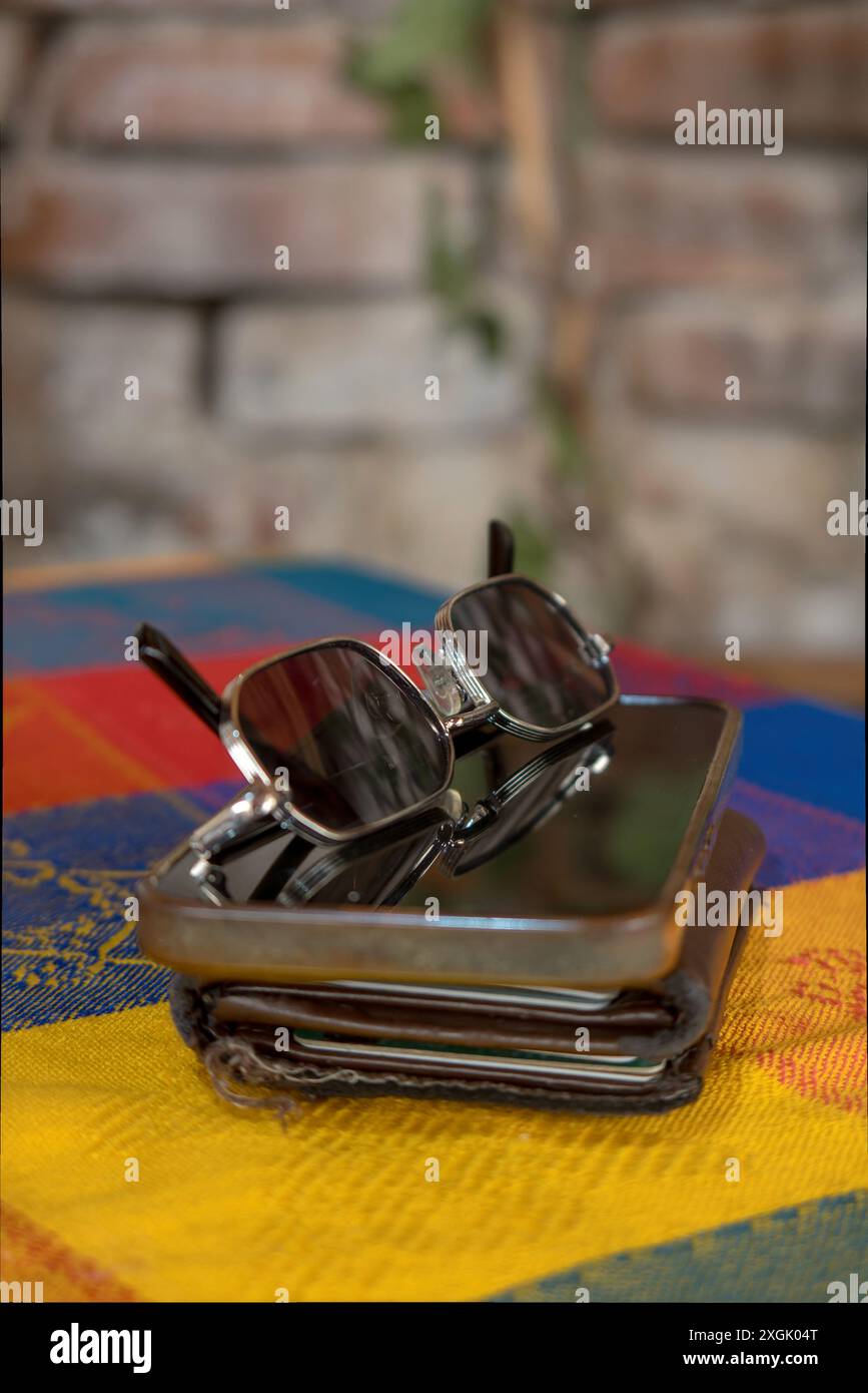 Primo piano di eleganti occhiali da sole appoggiati su smartphone e portafoglio, appoggiati su una parete rustica in mattoni. Perfetto per concetti di essenziale da viaggio, moderno Foto Stock