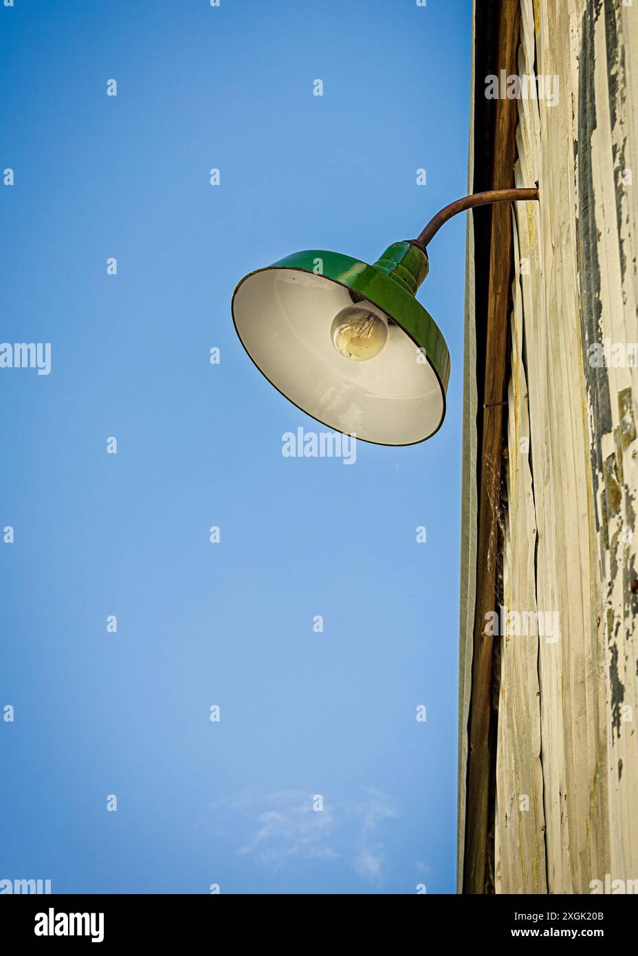 L'impianto di illuminazione industriale verde vecchio stile è appeso sul lato di un edificio con vernice scheggiata Foto Stock