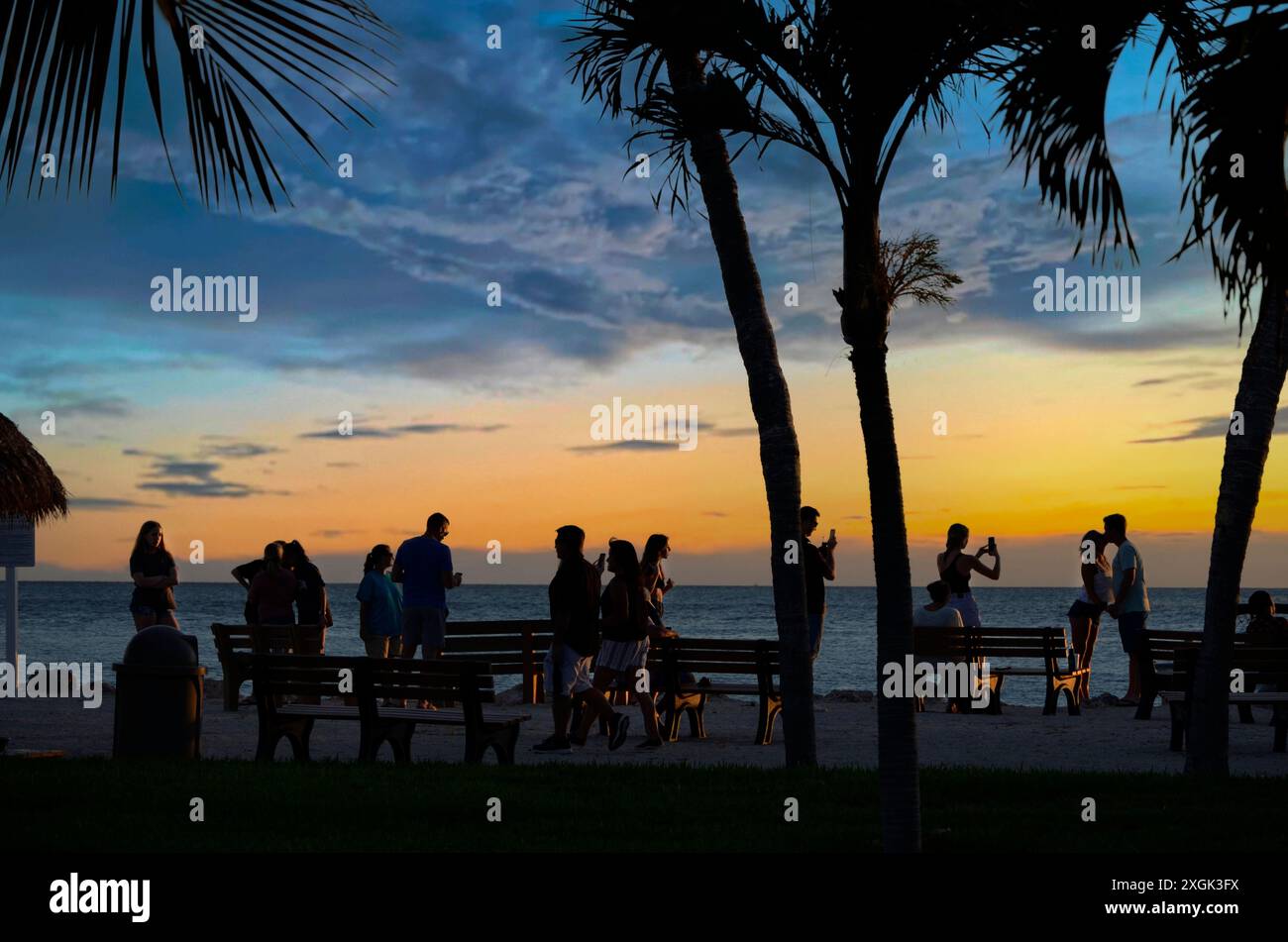 La gente si riunisce al tramonto per una festa in spiaggia sotto le palme dei Caraibi Foto Stock