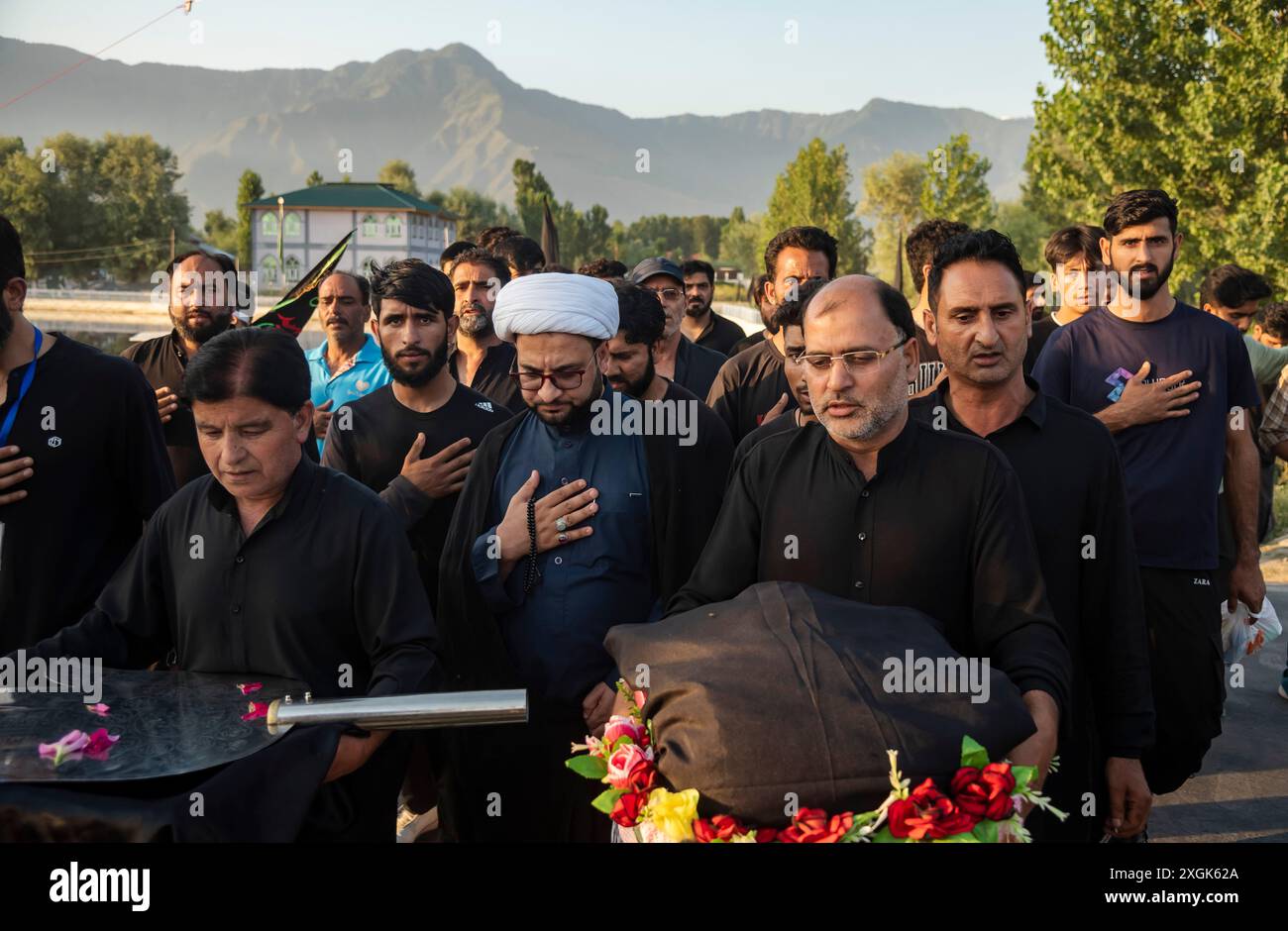 I musulmani sciiti del Kashmir picchiano il loro petto mentre recitano la poesia religiosa mentre si preparano a installare una grande bandiera religiosa su una strada durante Muharram. Muharram iniziò in Kashmir con profonda riverenza, specialmente tra la comunità musulmana sciita, commemorando il martirio dell'imam Hussain nella battaglia di Karbala. I primi dieci giorni, che culminano con l'Ashura, presentano processioni solenni in cui i lori vestiti di nero portano striscioni e eseguono ritmici battendo il petto. Si tengono raduni Majlis dove gli studiosi religiosi raccontano gli eventi di Karbala, e le recitazioni emotive di Marsiya sono comuni. Intri Foto Stock