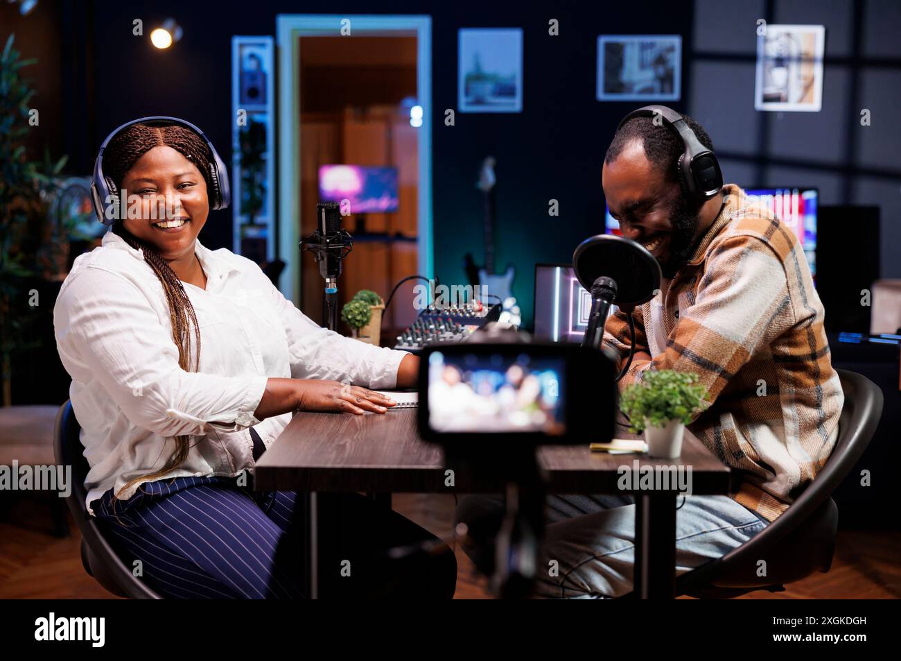 Influencer gioiosi in studio che utilizzano una fotocamera professionale per creare spettacoli comici per i canali in live streaming. Allegri protagonisti dei social media che lavorano insieme nella sessione di vlogging utilizzando apparecchiature video. Foto Stock