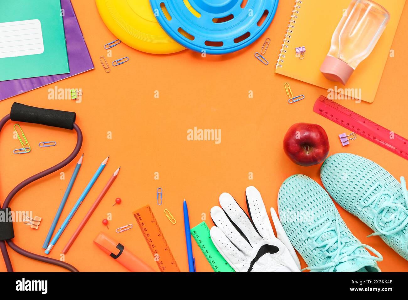 Telaio realizzato con sneakers, frisbee, mela, espansore e diversi articoli di cancelleria su sfondo arancione Foto Stock