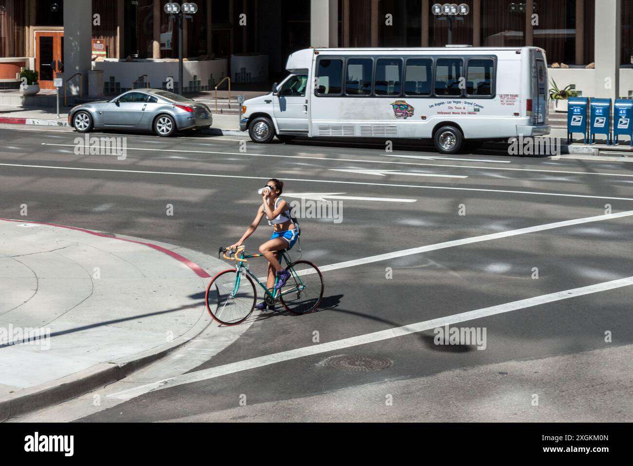 Donna che cavalca la sua bici attraverso una strada bevendo un caffè a Los Angeles Foto Stock
