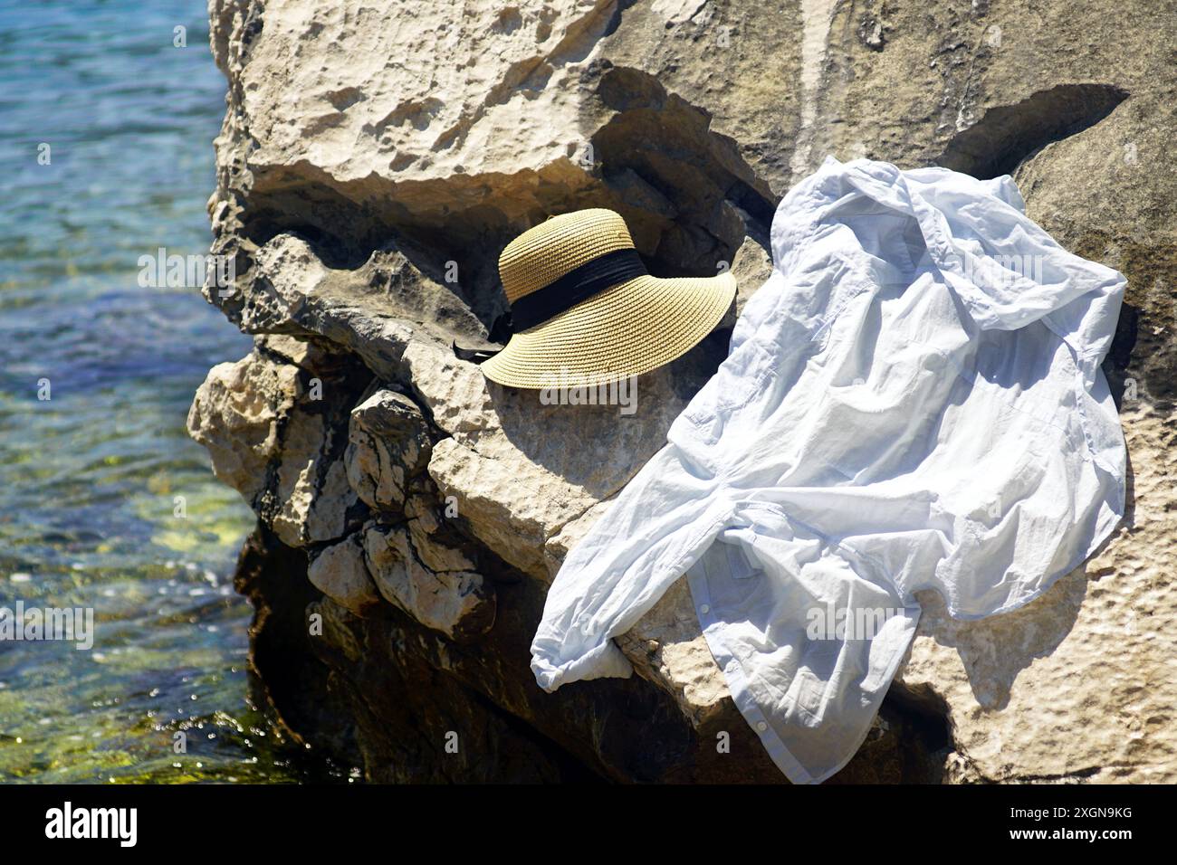 Un cappello da donna e una camicia leggera su una roccia vicino al mare. Vacanze estive in Montenegro - vestiti sdraiati sulla spiaggia, lasciati dietro da una turista femminile. Foto Stock