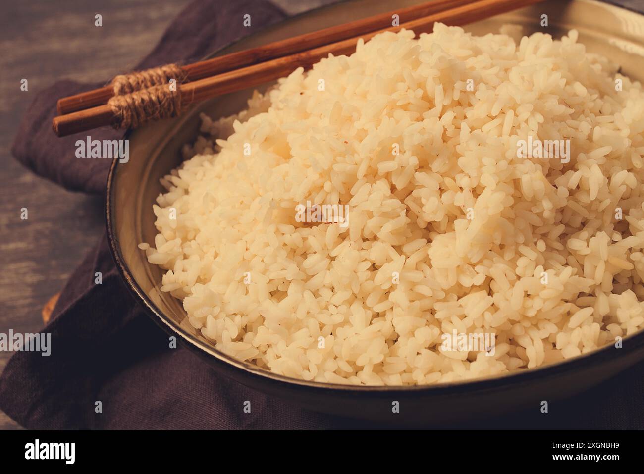 Un piatto di riso bollito, con bastoncini di legno, su fondo marrone, senza persone, messa a fuoco selettiva, tonificato Foto Stock