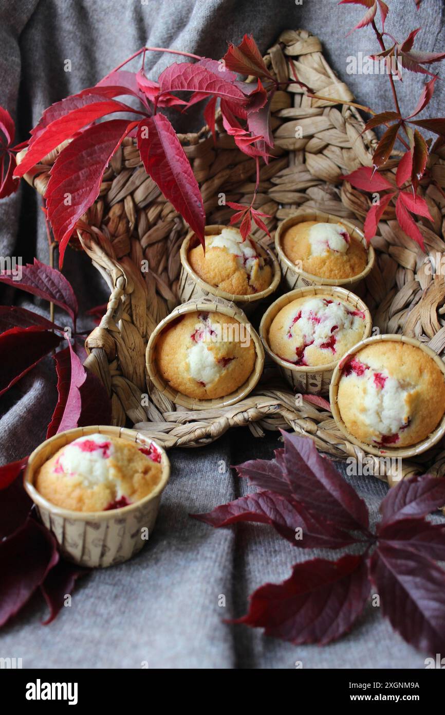 Muffin in un cestino intrecciato circondato da foglie rosse su un tessuto grigio che crea un'atmosfera rustica autunnale Foto Stock