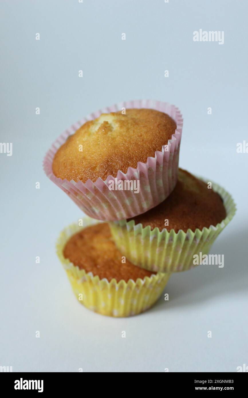 Tre muffin fatti in casa impilati con fodere di carta color pastello su sfondo bianco Foto Stock