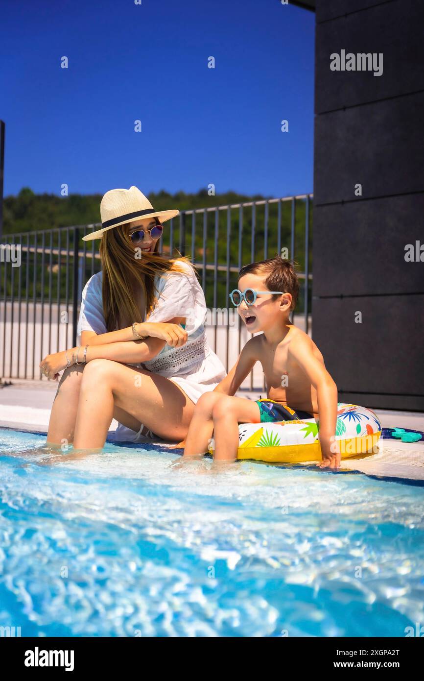 Foto verticale di una madre caucasica e di un ragazzo con anello di gomma seduti in piscina insieme Foto Stock