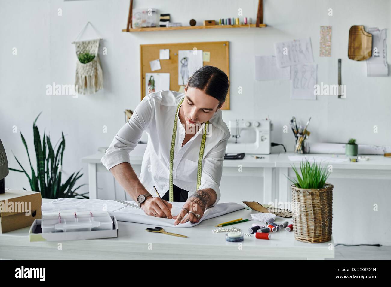 Un giovane disegna un motivo su un tavolo bianco nella sua officina, circondato da strumenti e materiali per il restauro dell'abbigliamento. Foto Stock