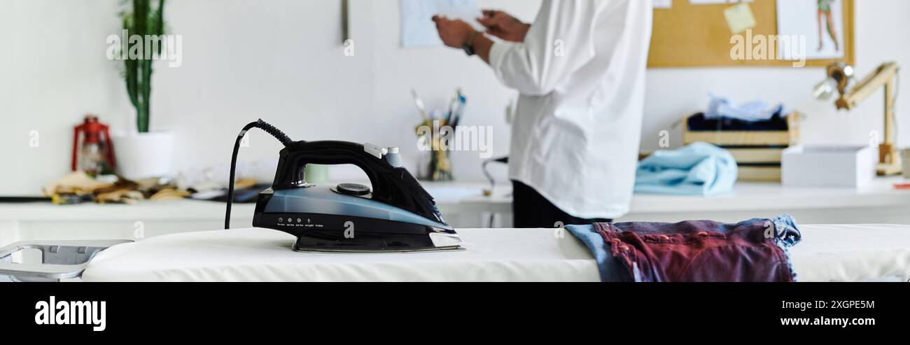 Un ferro da stiro si trova su un'asse da stiro in un atelier di restauro di abiti, pronto a dare nuova vita agli articoli scartati. Foto Stock