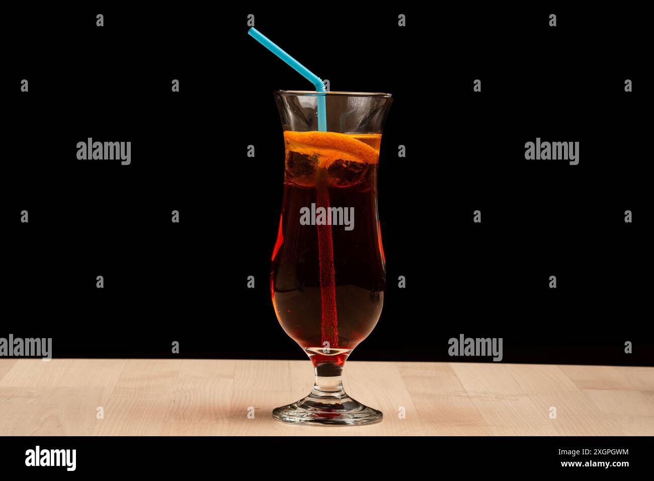 Un bicchiere di tè freddo con fette di limone e una paglia blu su un tavolo di legno su sfondo nero Foto Stock