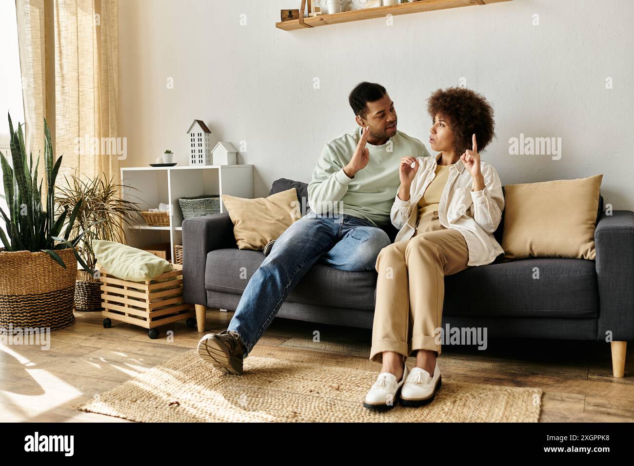 Una coppia si siede su un divano, usando il linguaggio dei segni per comunicare tra di loro. Foto Stock