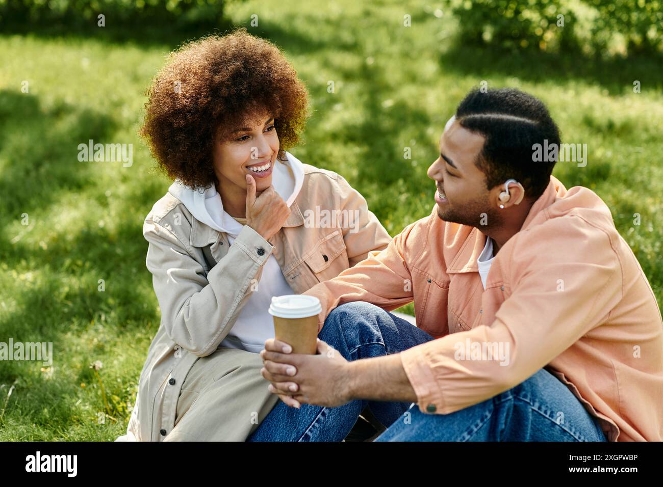 Una coppia si siede sull'erba, godendosi una giornata di sole mentre comunica in linguaggio dei segni. Foto Stock