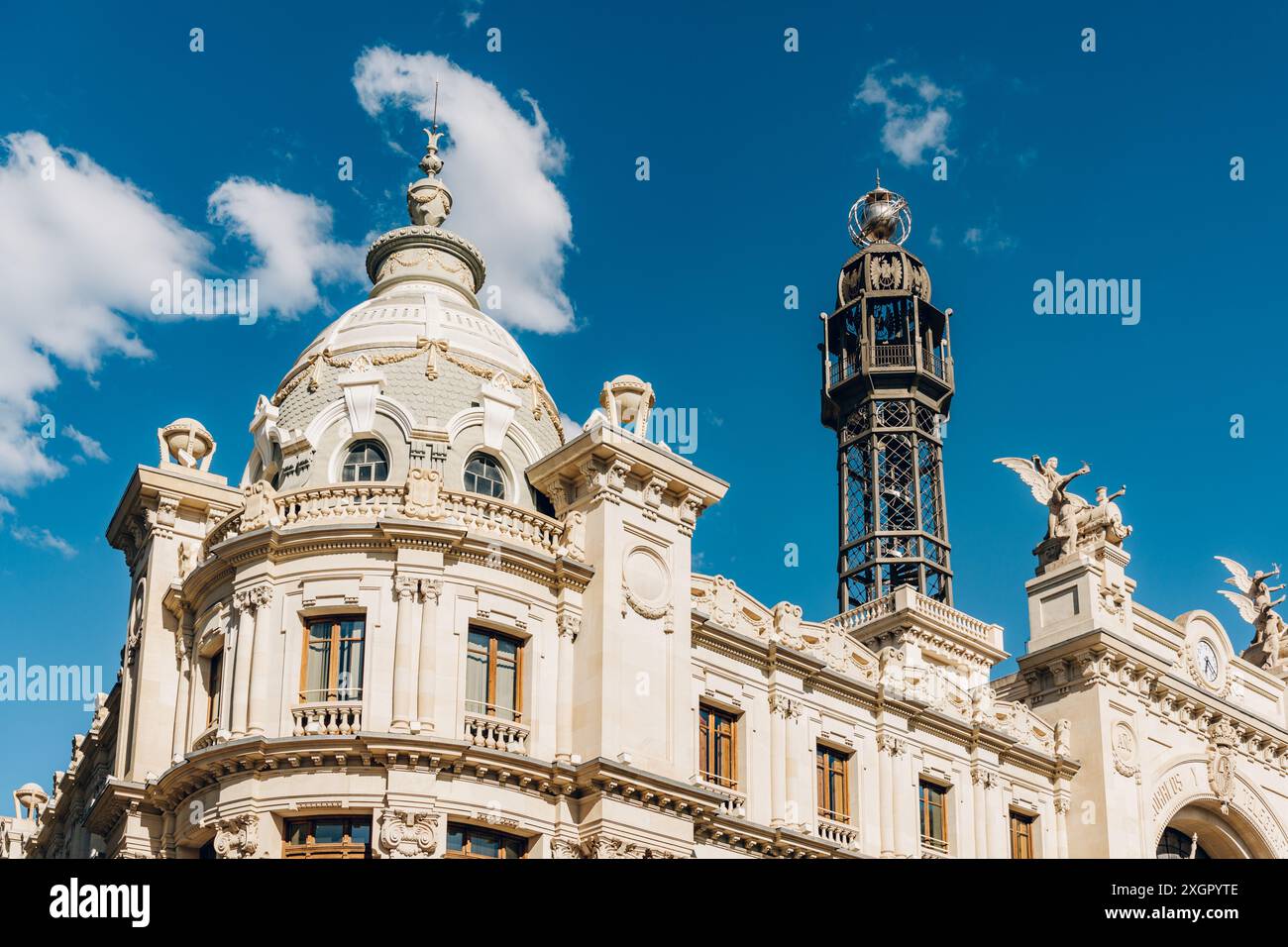Vista dettagliata di una cupola e di una torre ornata su un edificio storico di Valencia. Gli elementi architettonici e il cielo limpido sottolineano il ricco patrimonio e la grandiosità della città. Foto Stock