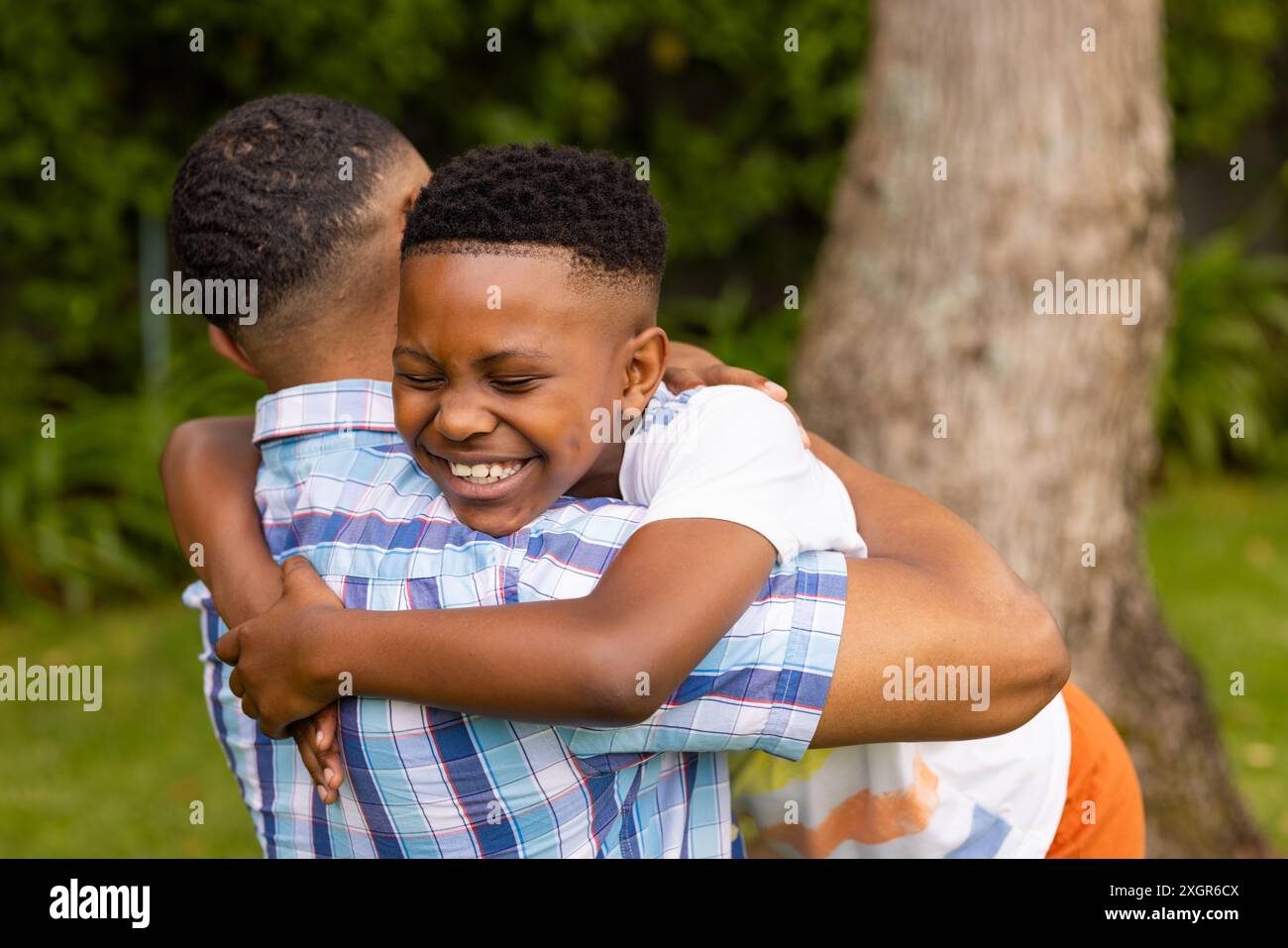 Un figlio afroamericano abbraccia il padre afroamericano all'aperto. Il loro caldo abbraccio trasmette un forte legame e un rapporto affettuoso. Foto Stock