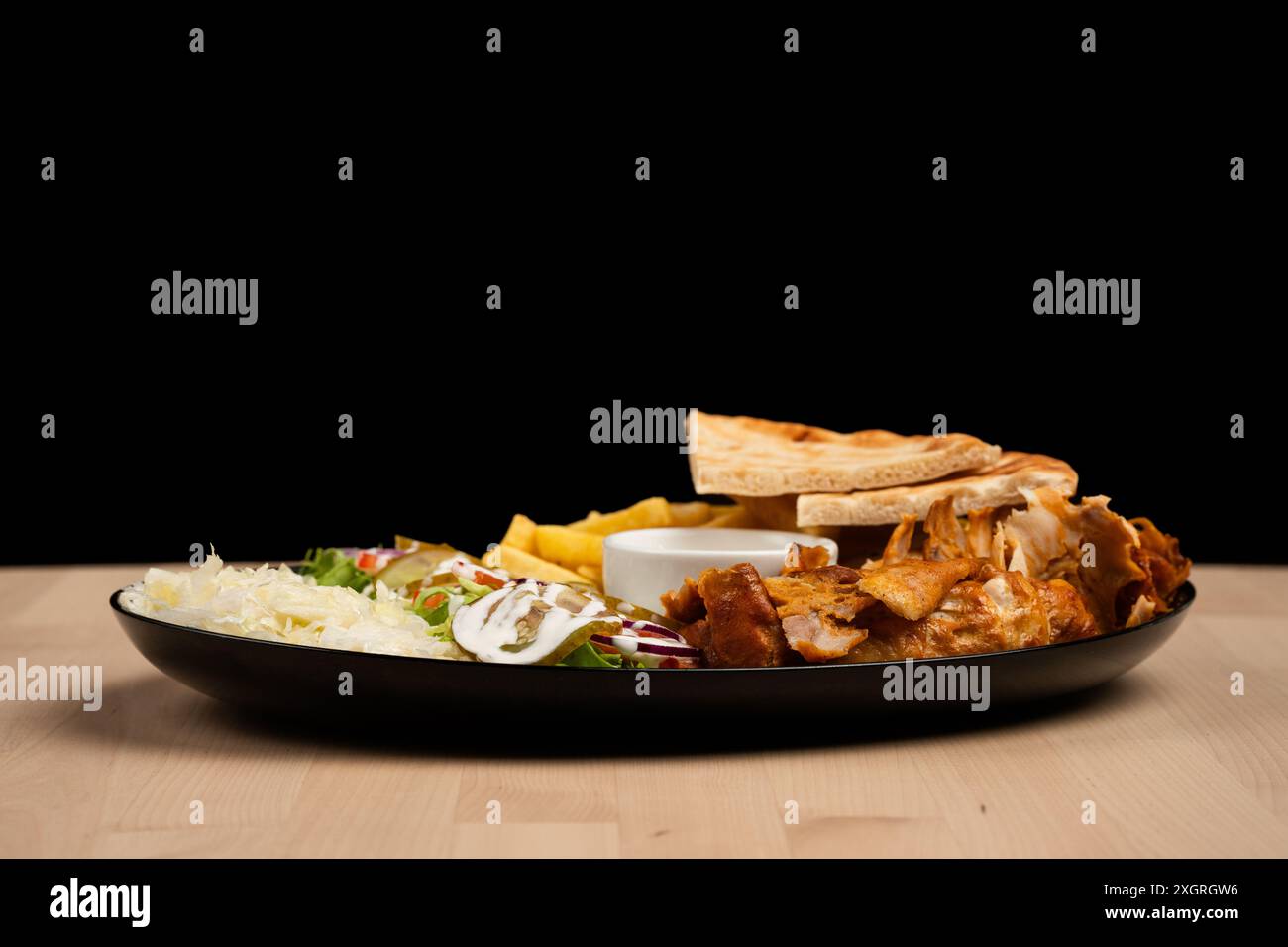 Un delizioso piatto di insalata mista, patatine fritte, pane pita, pollo e salsa su un tavolo di legno su sfondo nero Foto Stock
