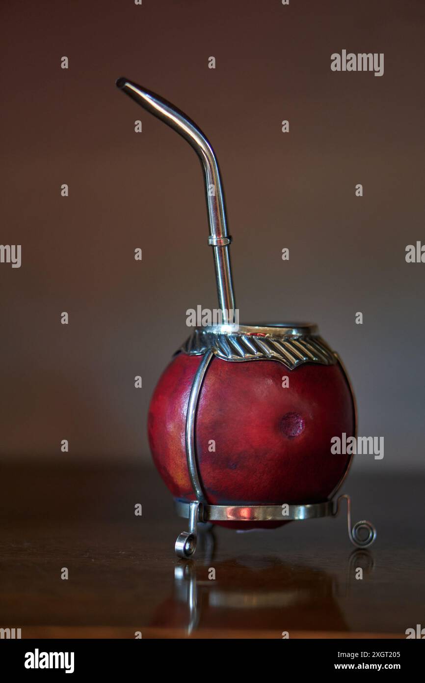 primo piano di un compagno rosso con bombilla in acciaio e dettagli in argento su un tavolo in legno, messa a fuoco selettiva. Foto Stock