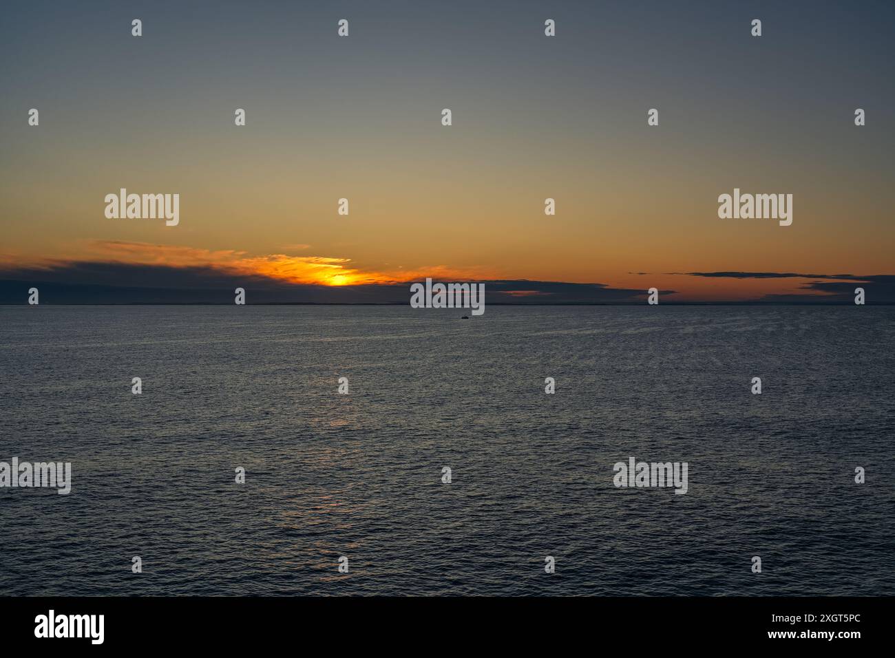 Una piccola barca da pesca solitaria naviga attraverso le calme acque del Mare dello Skagerrak, che sorge al sole e getta un bagliore dorato all'orizzonte vicino alla costa della Norvegia Foto Stock